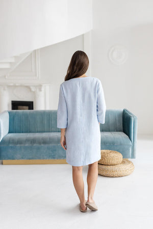 Back view of light blue linen shift dress, simple design, with blue sofa and white decor.