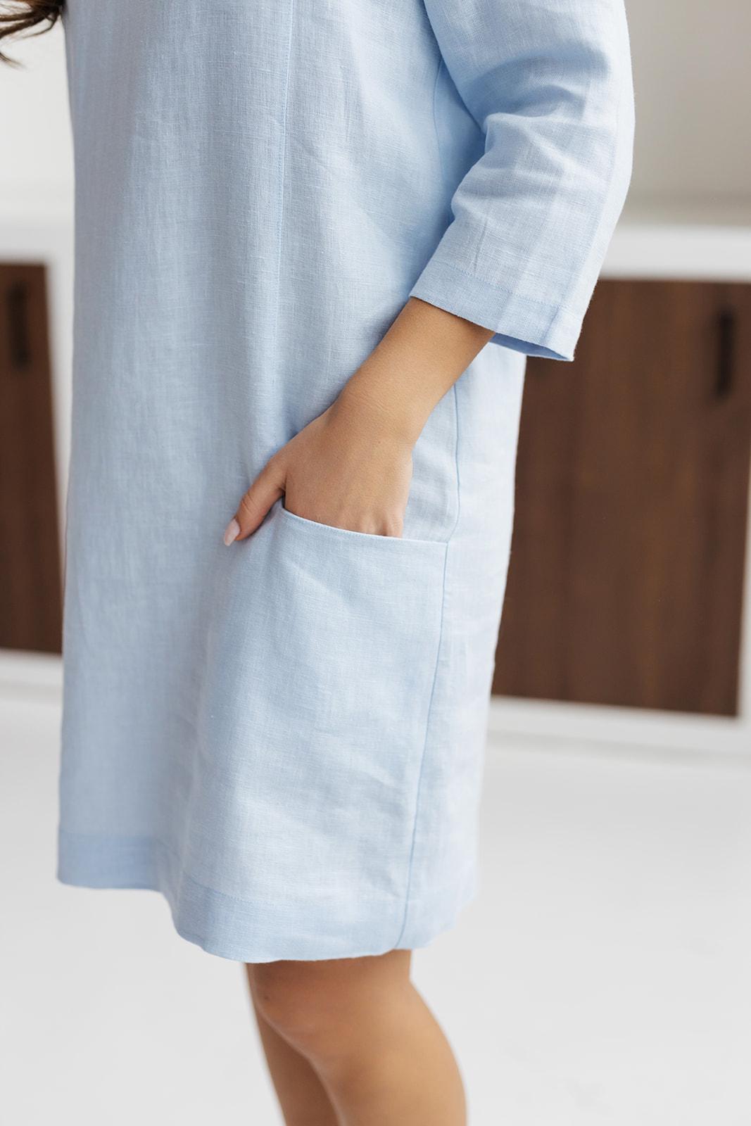 Close-up of light blue linen shift dress, showing front pockets and linen fabric texture.