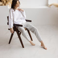 Model seated on wooden chair, wearing dusty gray straight-leg relaxed fit linen pants and white linen top.