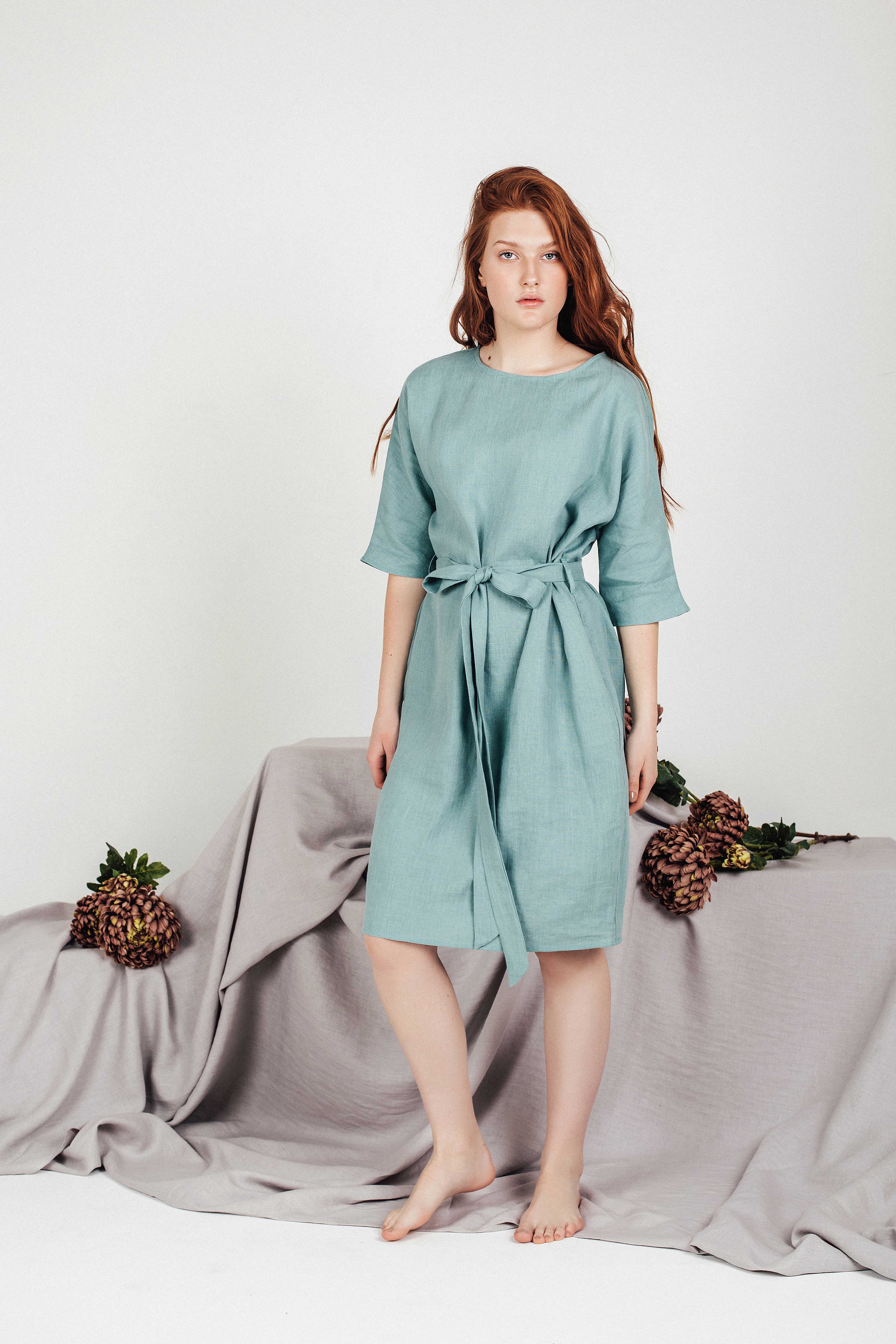Full-body studio shot of a model wearing the LIRA sea-green linen tunic dress by Sonfre, demonstrating the relaxed fit, tied waist, and boat neckline.