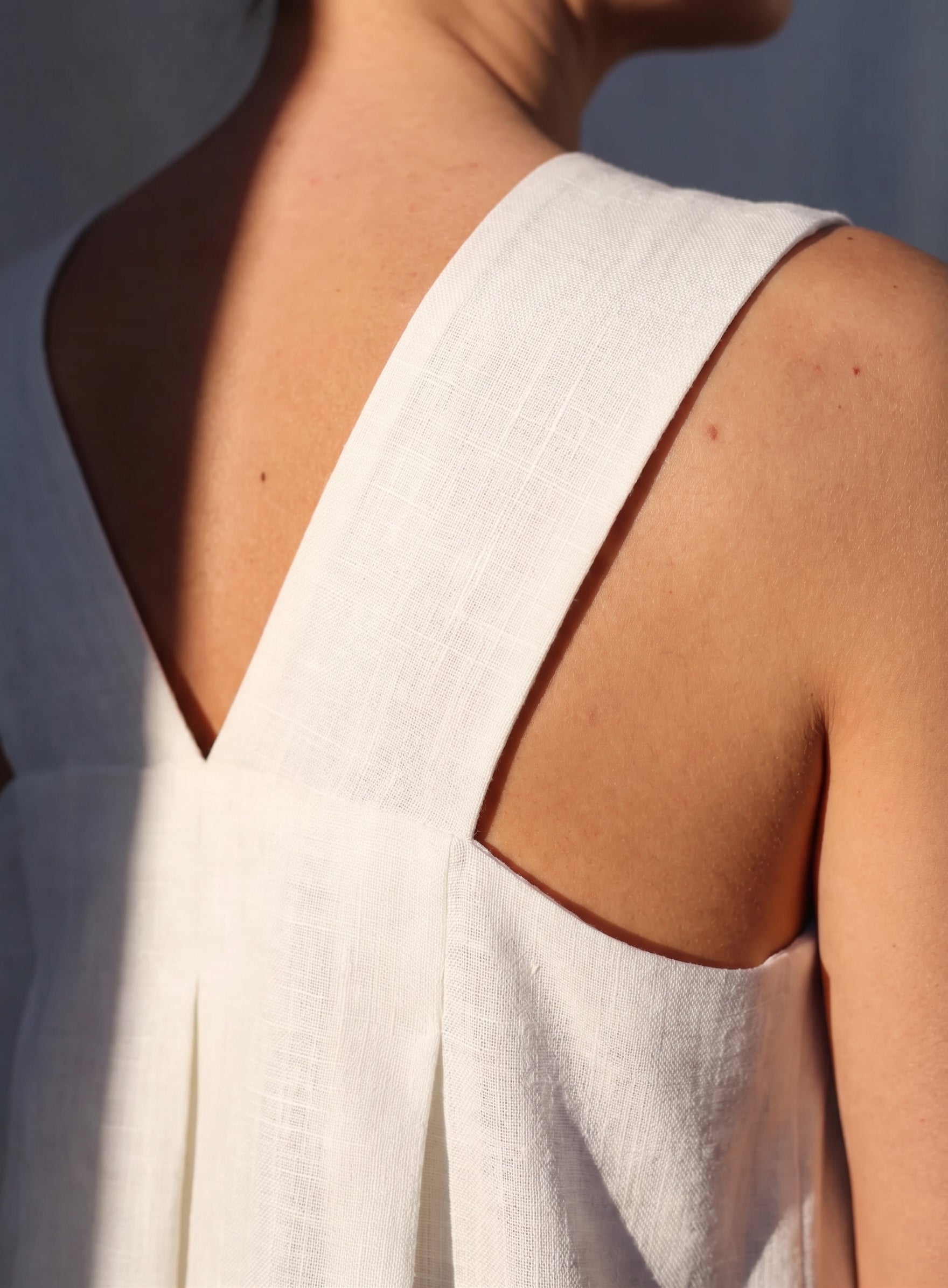 Macro close-up of the SonFre ONA white linen dress showing the high-quality woven fabric texture, sturdy wide shoulder strap, and back pleat detail.