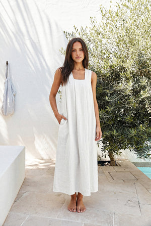 Model wearing the SonFre ONA sleeveless white linen trapeze maxi dress with a square neck and side pockets, standing outdoors.