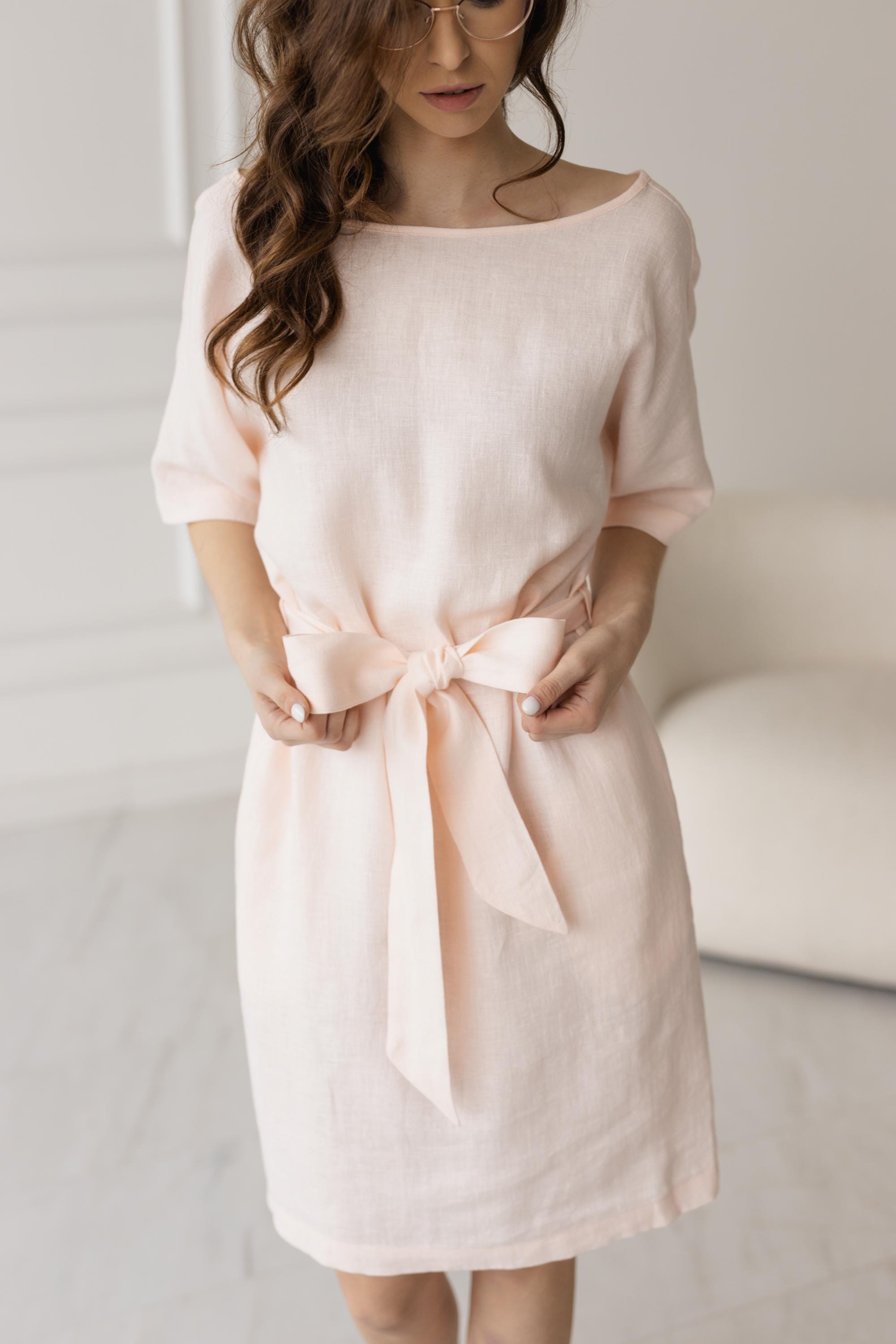Close-up of petal pink tie-waist shift dress, bow detail, soft linen fabric.