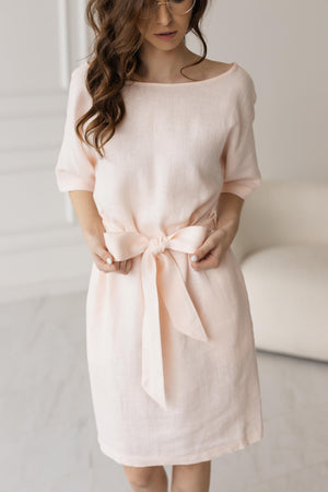 Close-up of petal pink tie-waist shift dress, bow detail, soft linen fabric.