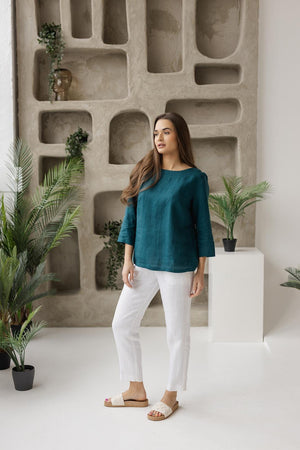 Model in teal green linen boat neck blouse, mid sleeves, styled with white pants, casual minimalist look