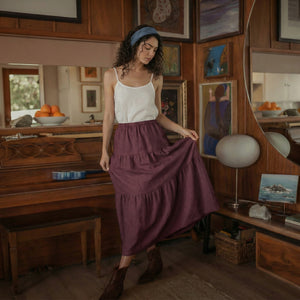 Woman wearing a grape wine linen tiered skirt with functional deep side pockets.