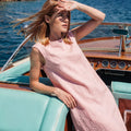 Woman wearing the VELA dusty rose linen shift dress while lounging on a vintage wooden boat in the Mediterranean.