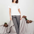 Front view of woman wearing white boxy linen top paired with grey linen pants