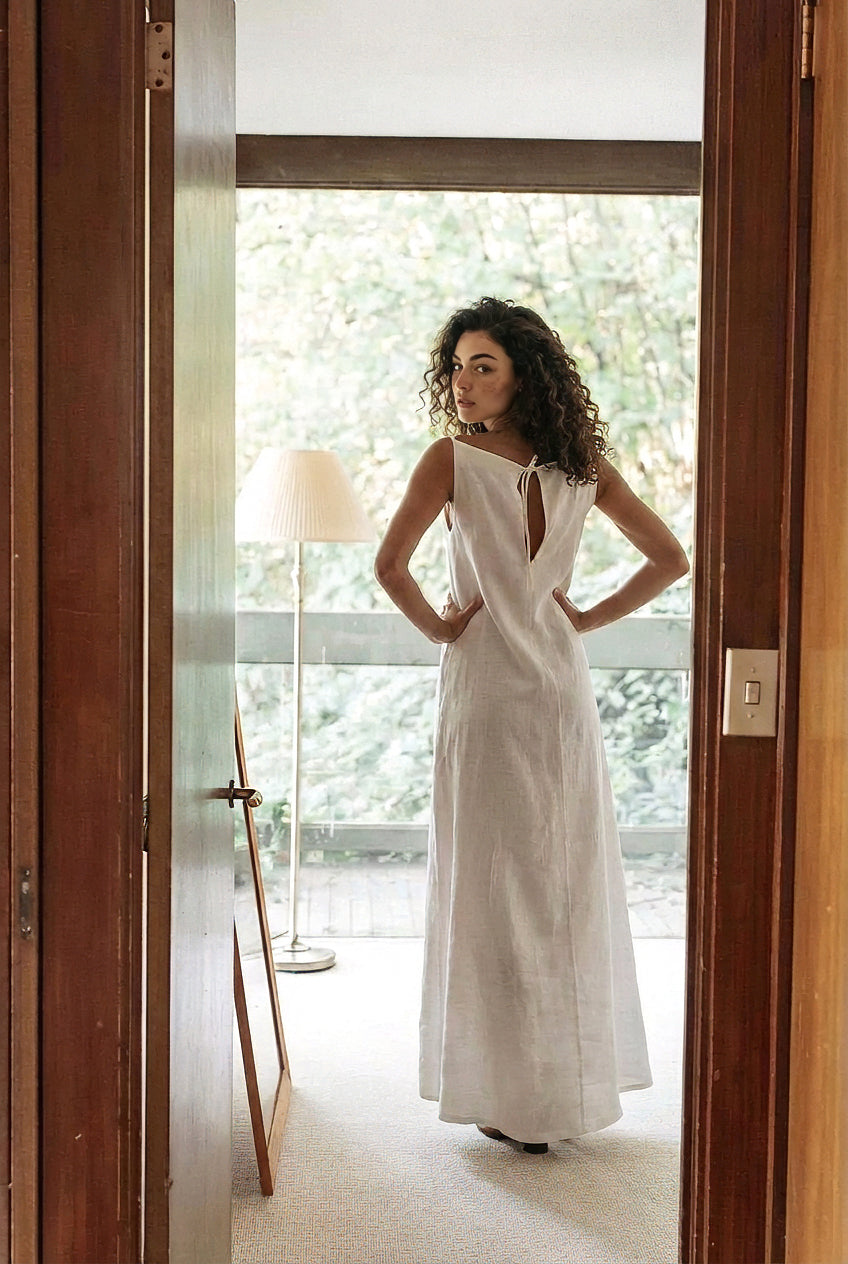Back view of sleeveless white linen gown showing feminine open back and tie closure detail.