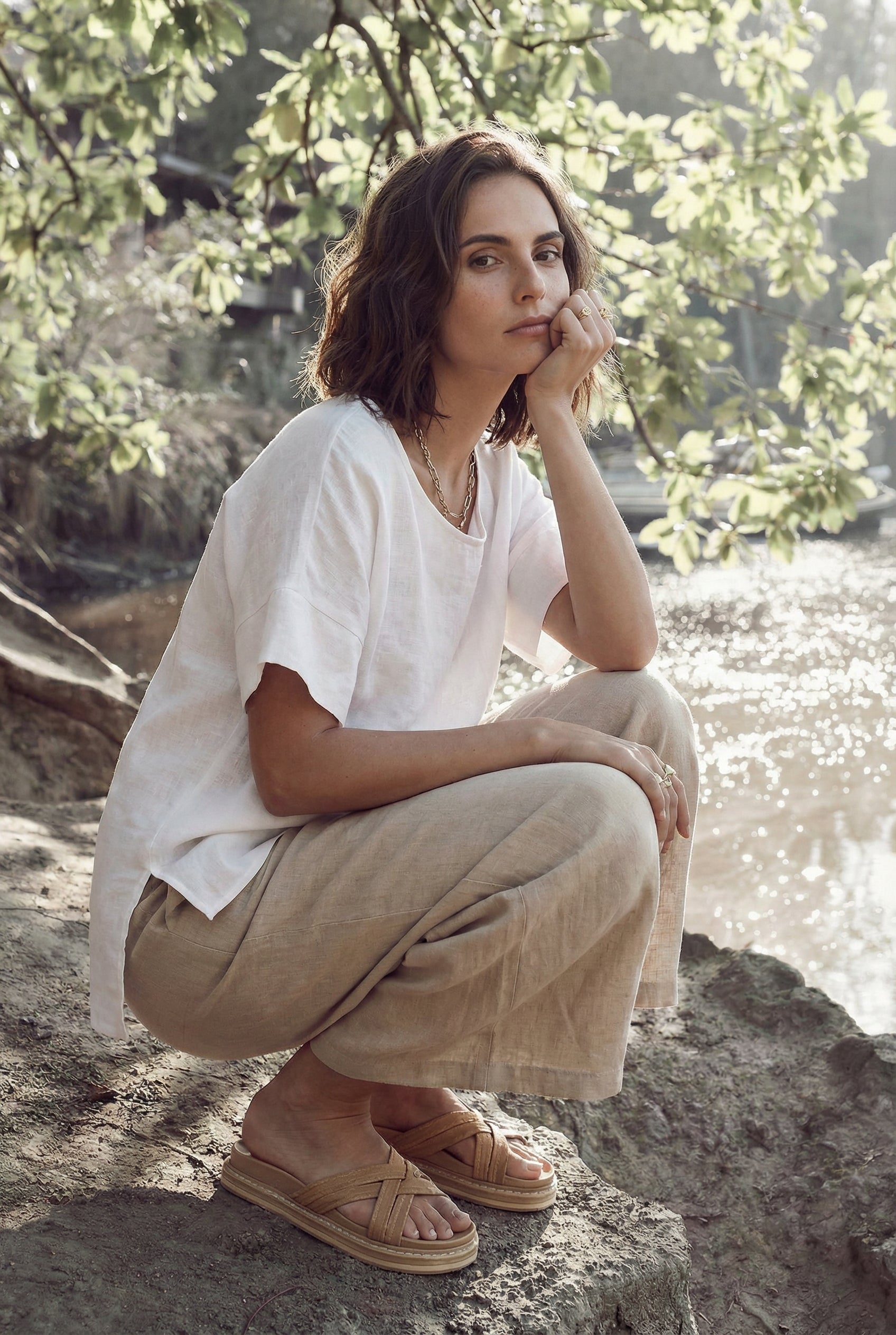 Woman crouching by a river wearing an effortless white linen tunic top with short sleeves.