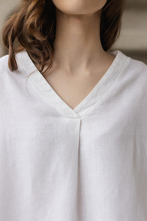 Close-up: white linen tunic fabric texture, V-neck detail. Soft, medium-weight linen.