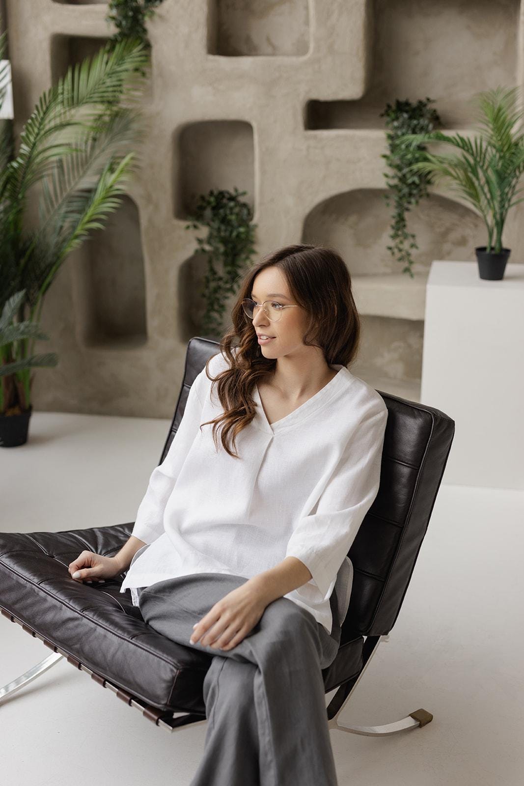 Woman seated, wearing white linen tunic. Loose fit, 3/4 sleeves. Relaxed pose.