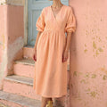 Woman wearing the JOLA handmade peach linen surplice midi dress, featuring a V-neck faux-wrap bodice, gathered skirt, and 3/4 balloon sleeves.